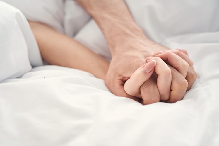 Capricorn couple holding hands in bed.