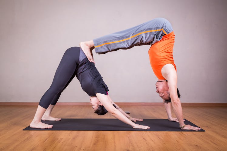 2 person yoga poses include a double downward dog by a couple within a studio.