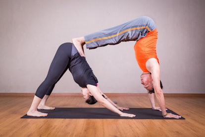2 person yoga poses include a double downward dog by a couple within a studio.
