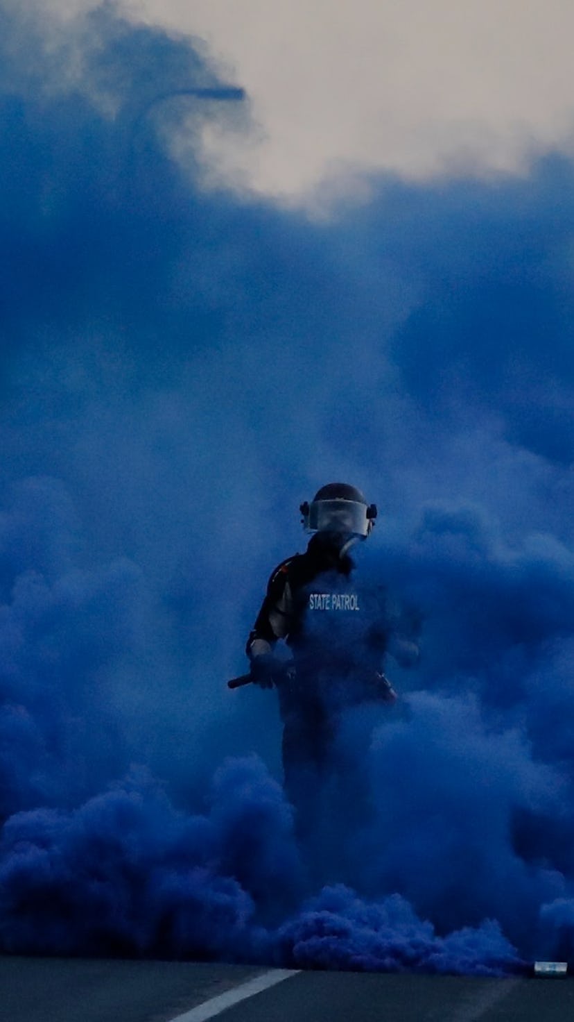 Police in riot gear walk through a cloud of blue smoke as they advance on protesters near the Minnea...