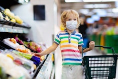 Shopping with kids during virus outbreak. Child wearing surgical face mask buying fruit in supermark...