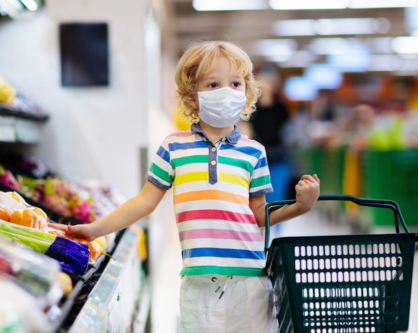 Shopping with kids during virus outbreak. Child wearing surgical face mask buying fruit in supermark...