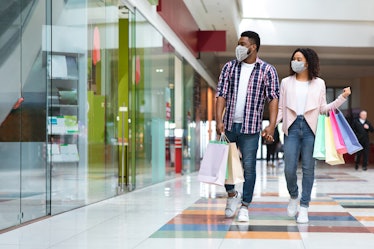 Pandemic Shopping. Black couple wearing protective face medical masks walking with shopper bags in m...