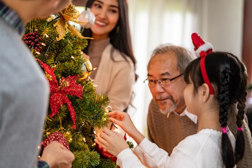 Multigenerational asian Family decorating a Christmas tree. Mom Dad daughter girl and grandfather de...