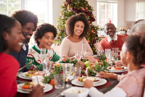 Happy multi generation mixed race family sitting at their Christmas dinner table eating and talking,...