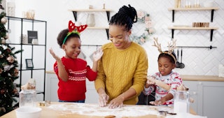 Cheerful African American woman in apron with little kids standing at table in home Christmassy deco...