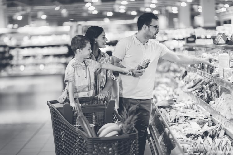 Family with child and shopping cart buying food at grocery store.
