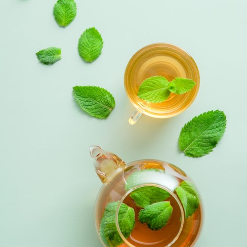 Mint tea. Flat lay, top view teapot and tea cup with mint leaves on green background.
