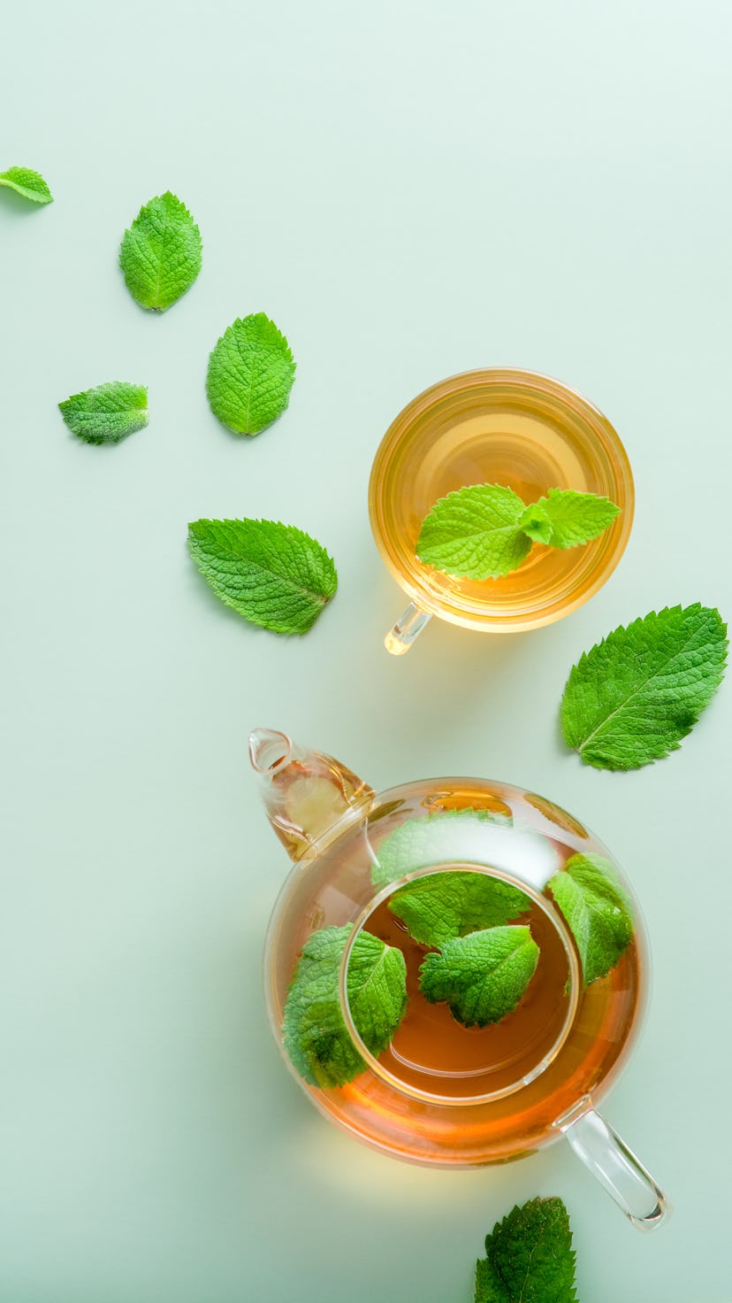 Mint tea. Flat lay, top view teapot and tea cup with mint leaves on green background.