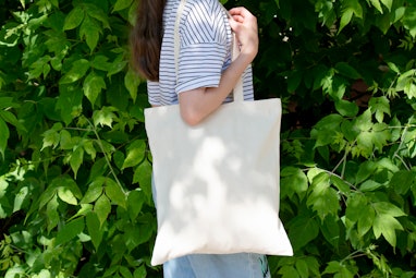 Empty reusable canvas tote bag mockup. Natural canvas eco-friendly shopper bag on girl's shoulder. M...