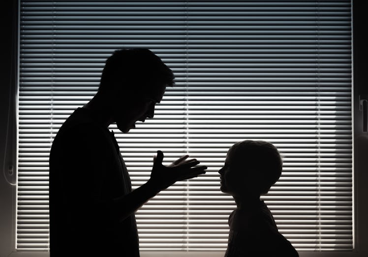 A frustrated dad scolds his kid; they are in shadows against a window
