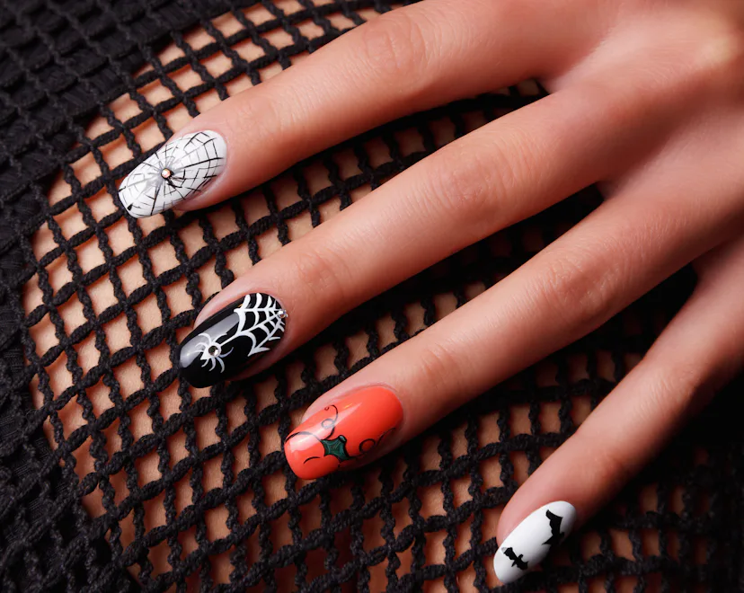 These Halloween nails feature orange, black, and white designs with spiderwebs, bats, and swirls.