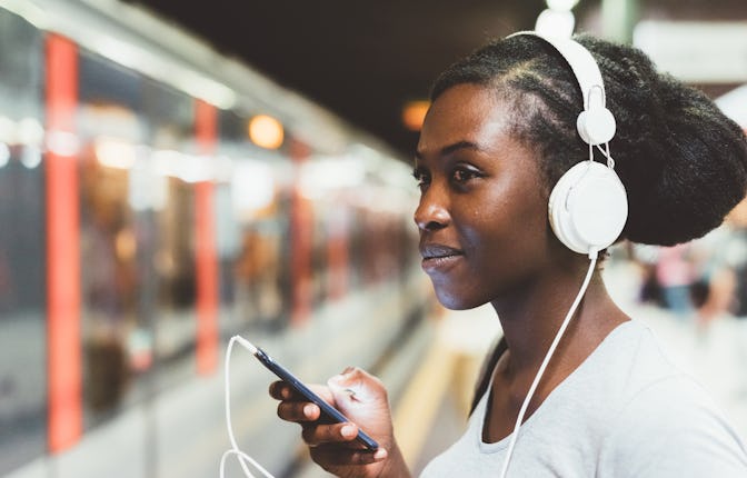 Half length of young beautiful afro black woman traveling on underground, listening music with headp...