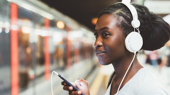 Half length of young beautiful afro black woman traveling on underground, listening music with headp...