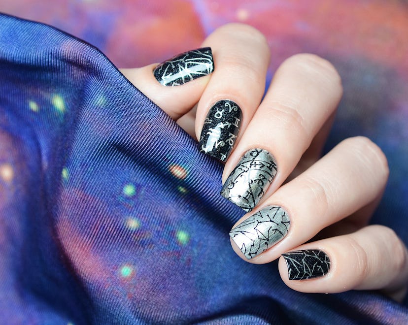 Black and silver manicure with a constellation map pattern on a cosmic background, representative of...