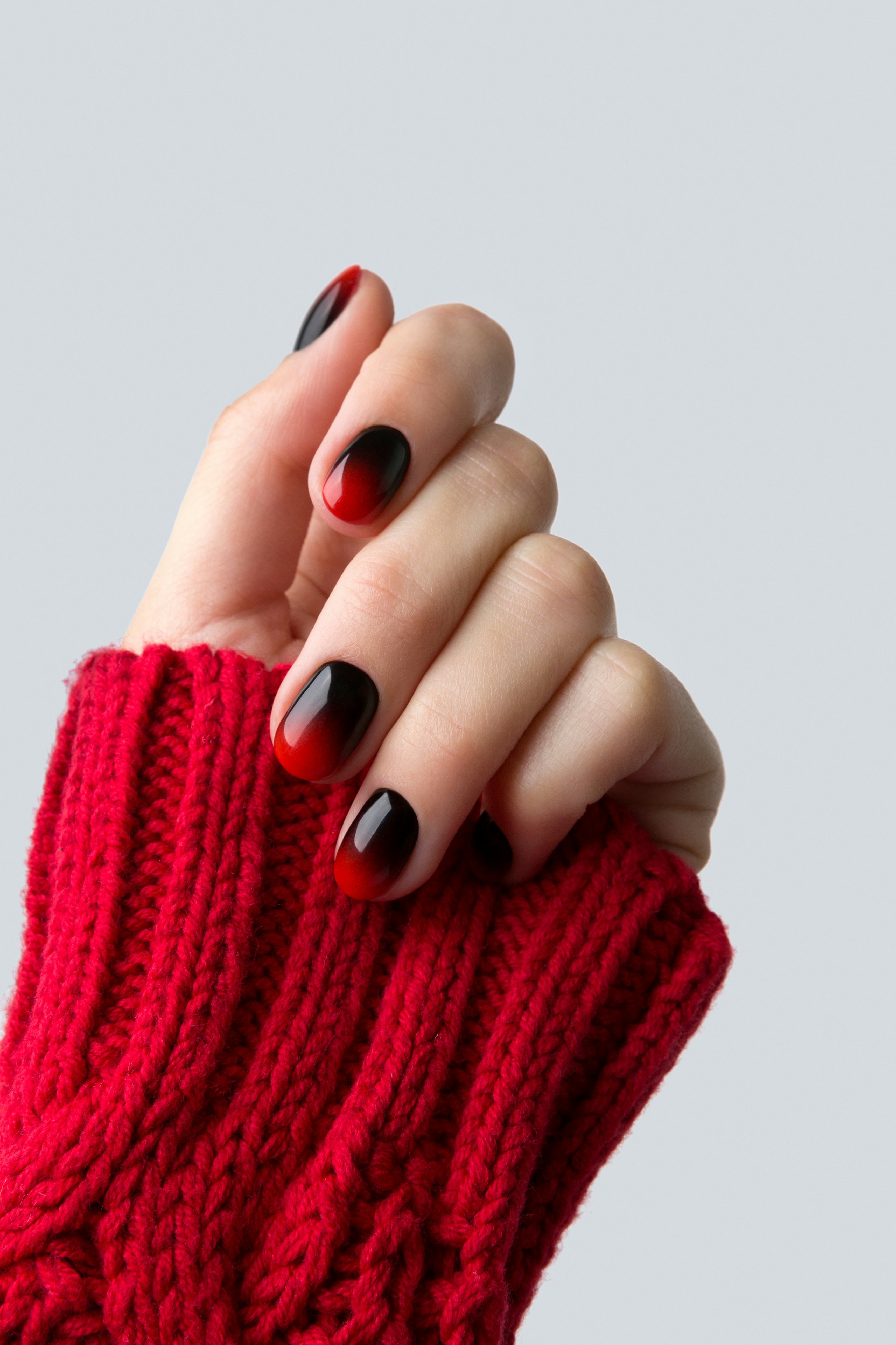 Female hand with red black ombre gradient nails in sweater. Trendy winter manicure concept.