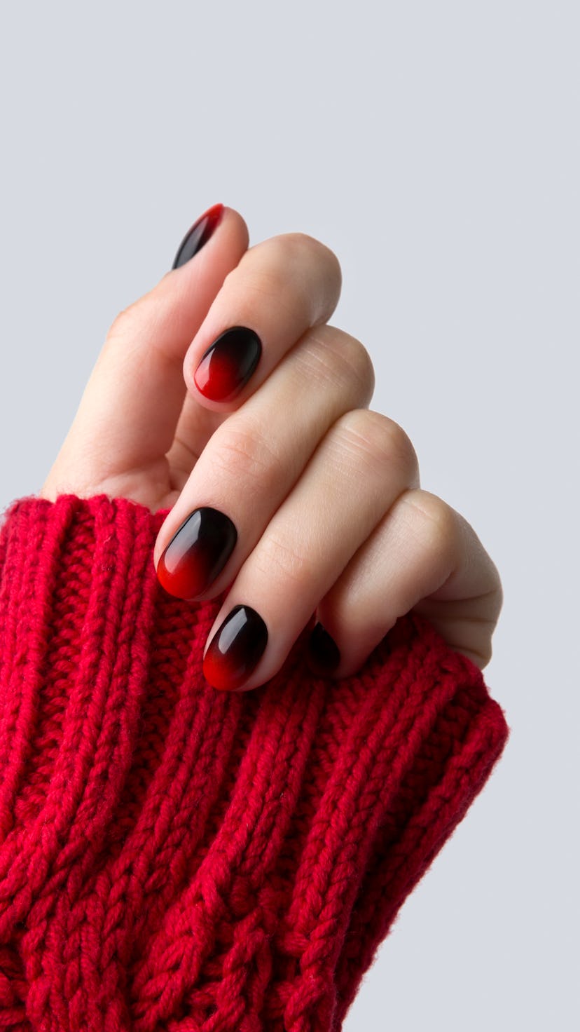 Female hand with red black ombre gradient nails in sweater. Trendy winter manicure concept.
