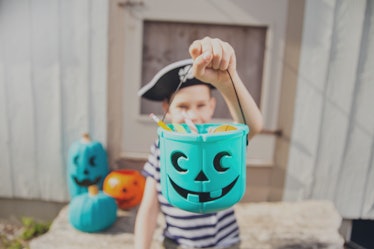 boy in a pirate costume holds a bucket with inedible gifts.  Teal Pumpkin Project. Halloween Allergy...