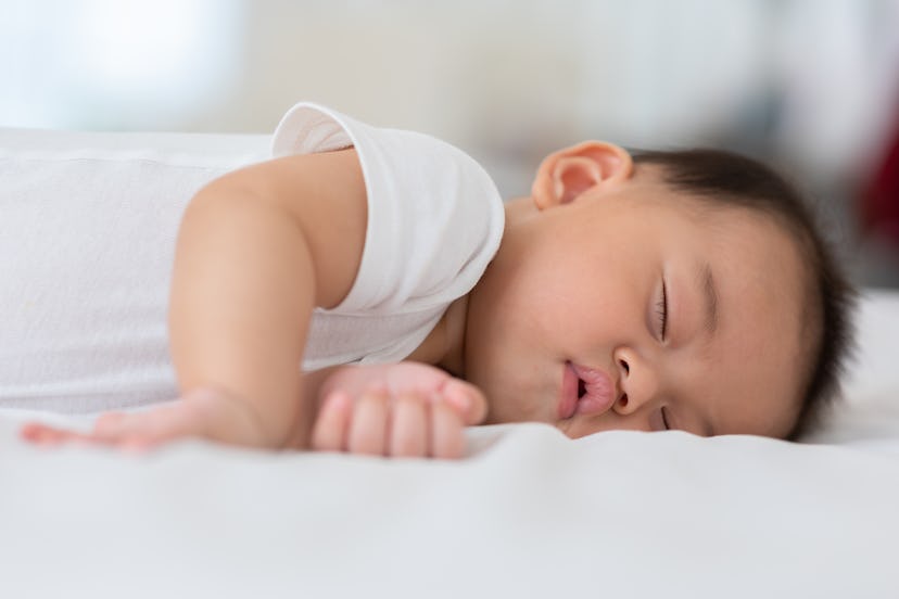 Happy asian newborn baby lying sleeps on a white bed in article about boy names that start with I