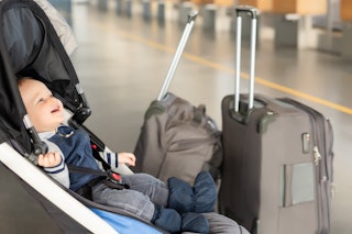 Cute funny caucasian baby boy sitting in stroller near luggage at airport terminal. Child sin carria...