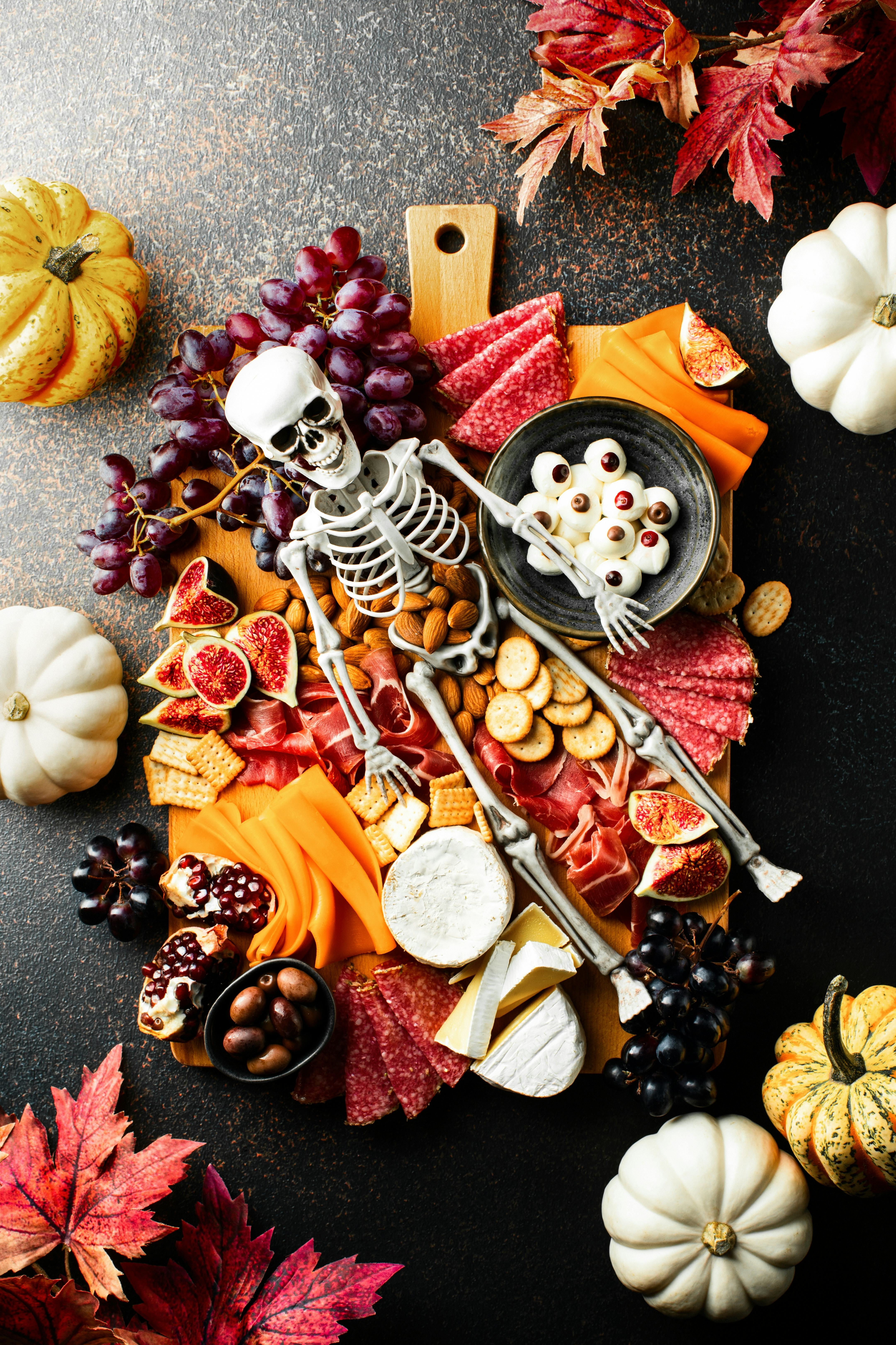 Halloween dark  table setting with cheese board decorated with spooky scary skeleton and pumpkins, t...