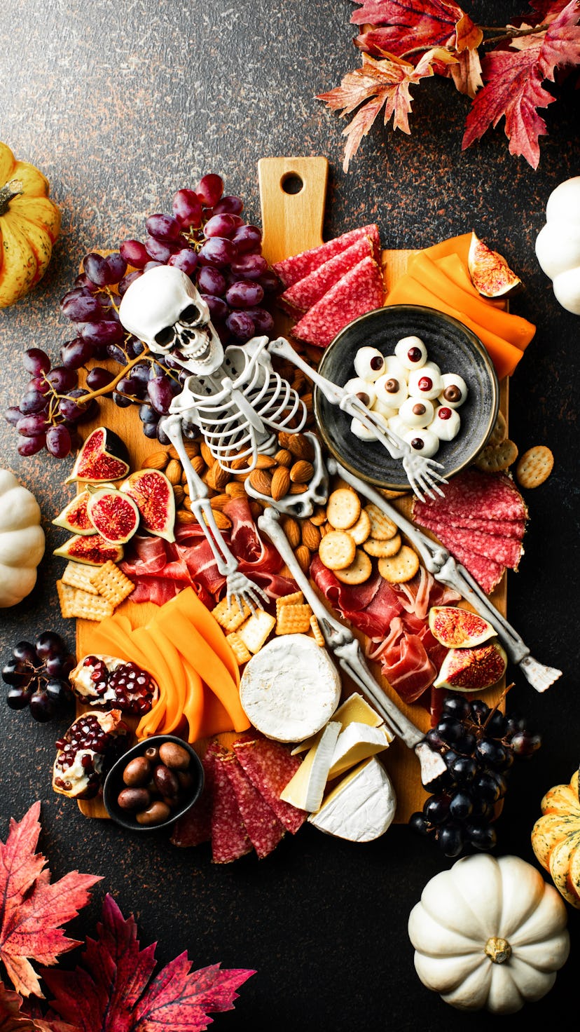 Halloween dark table setting with cheese board decorated with spooky scary skeleton and pumpkins, t...