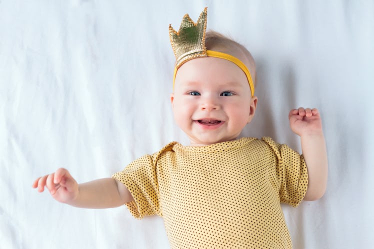 Portrait of happy 4-months-old baby girl lying on the white sheet in bed at home. The girl has a hea...