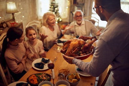 Close-up of man brining roast turkey at dining table while celebrating Thanksgiving with his family ...