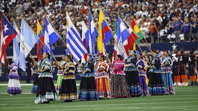 Women in costumes hold flags during the National Anthem as part of Hispanic Heritage month prior to ...