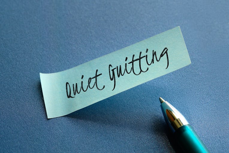 Text words Quiet Quitting on mint green paper note with pen on blue paper. Close-up on sticky note. ...