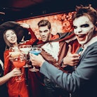 Friends in Halloween Costumes Drinking Cocktails. Group of Young Happy People Wearing Costumes at Ha...