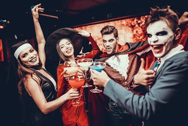 Friends in Halloween Costumes Drinking Cocktails. Group of Young Happy People Wearing Costumes at Ha...