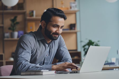 Smiling Indian business man working on laptop at home office.