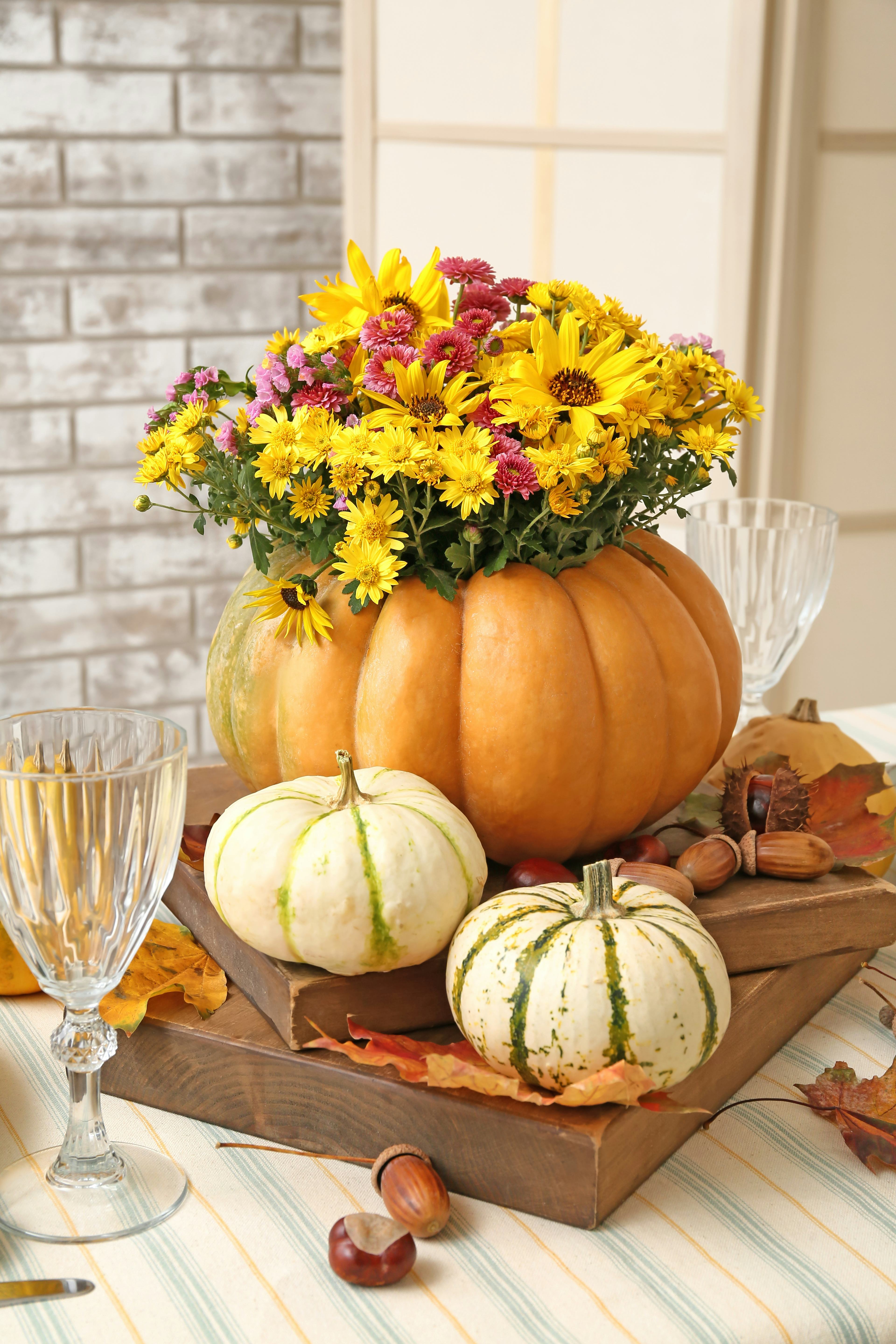 A pumpkin flower arrangement with wildflowers inside of an orange gourd on a table with small white ...