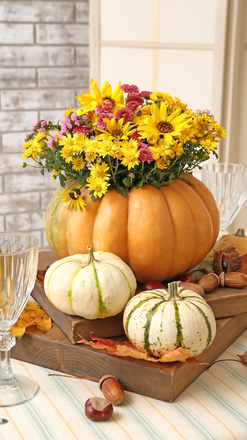 A pumpkin flower arrangement with wildflowers inside of an orange gourd on a table with small white ...