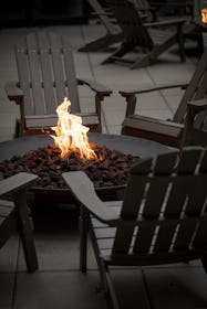 Side view on a dark fire pit, with orange flames, surrounded by a circle of Adirondack chairs