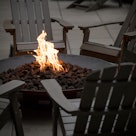 Side view on a dark fire pit, with orange flames, surrounded by a circle of Adirondack chairs