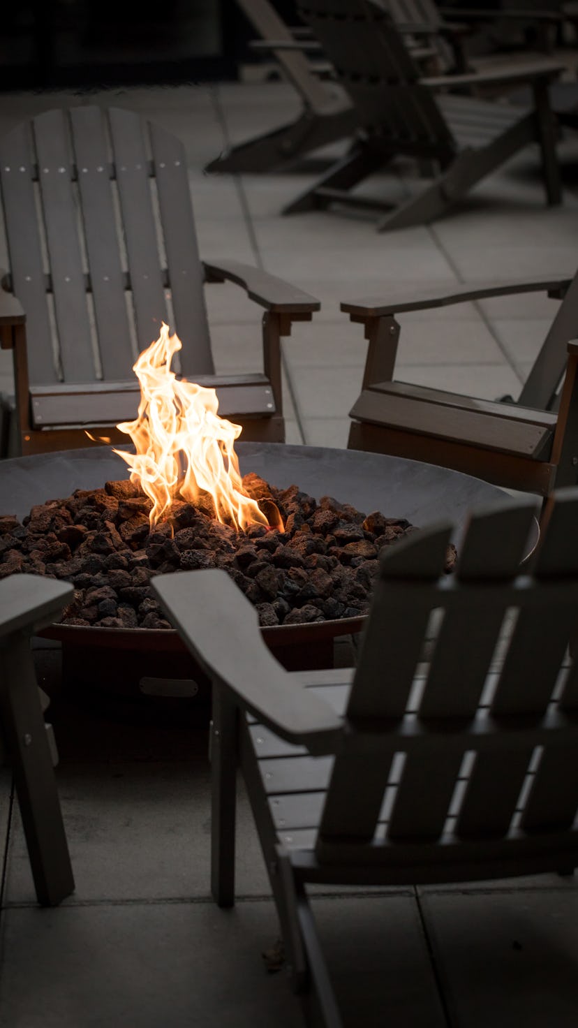 Side view on a dark fire pit, with orange flames, surrounded by a circle of Adirondack chairs