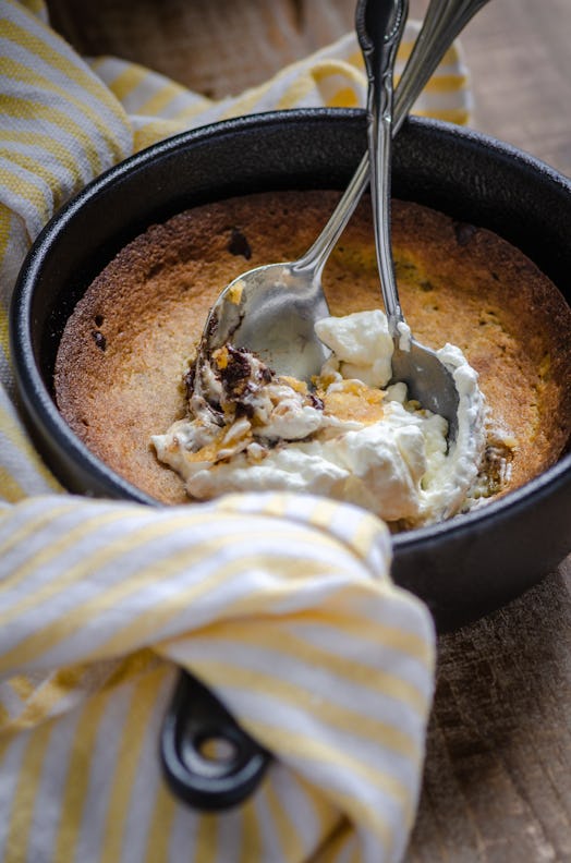 A cast iron skillet with a chocolate chip cookie baked inside, topped with whipped cream and two spo...
