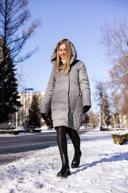 A woman in a winter down jacket and leather boots walks down a snowy street. Women's leather winter ...