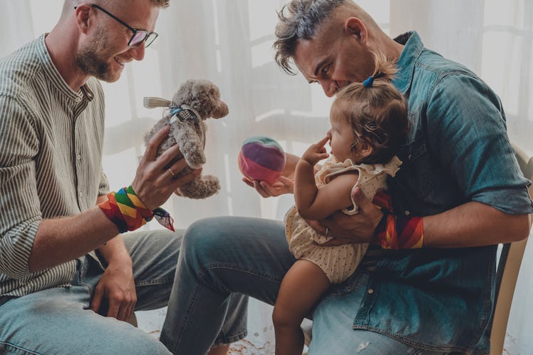 Gay couple with adopted baby girl playing at home.