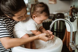 A mom washes her baby's hands in the sink, though sometimes exposing baby to germs can be beneficial...