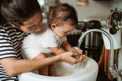 A mom washes her baby's hands in the sink, though sometimes exposing baby to germs can be beneficial...