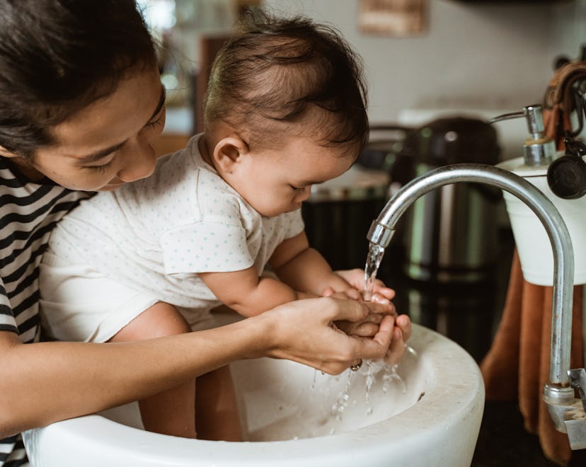 A mom washes her baby's hands in the sink, though sometimes exposing baby to germs can be beneficial...