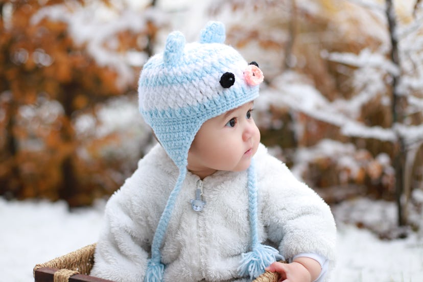 Close up of baby in a blue and white hat and fluffy jacket in the snow, in an article about winter s...