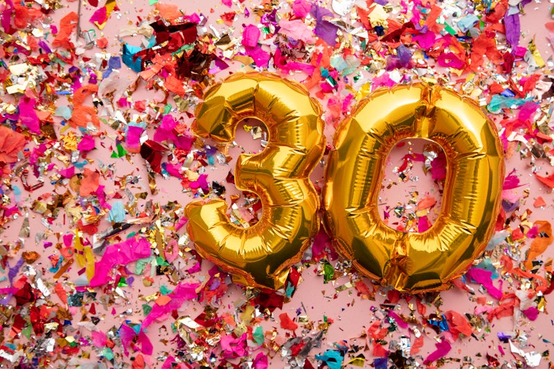 Number 30 gold birthday celebration balloon on a confetti glitter background