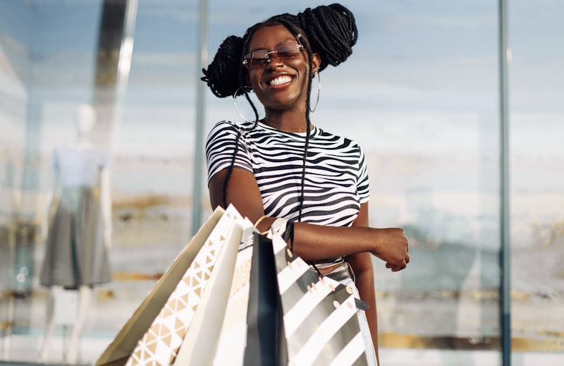 Happy young African American woman shopping with shopping bags and sunglasses, beautiful fashionable...