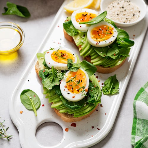 Healthy toast with sliced avocado, boiled eggs, spices and fresh spinach. Delicious breakfast or sna...