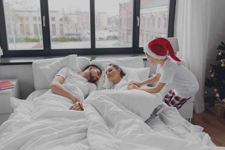 family, winter holidays and people concept - happy little son wakes his mother and father in christm...