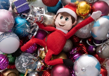Elf on the shelf being naughty playing in a ball pond of christmas baubles. Cute tradition of sendin...